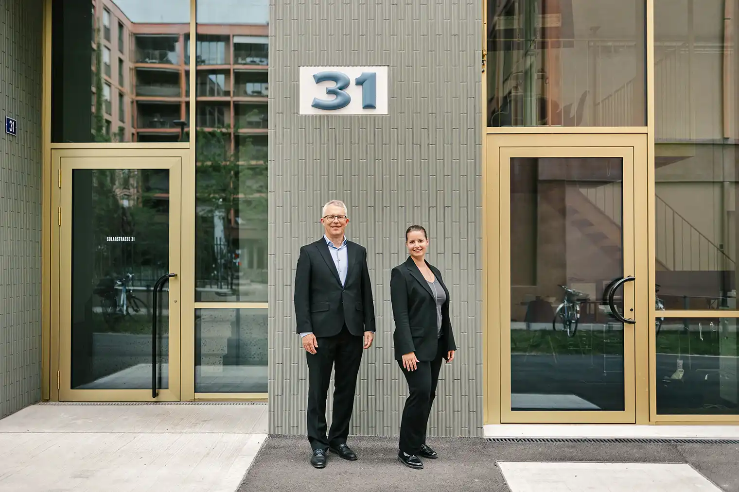 Foto zeigt Rolf Benz und Silvy Gillhausen, die vor ihrem neuen Büro in Winterthur-Neuhegi stehen. Der Bildlink führt auf die Seite Angebot.